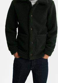 Tmavě zelená fleecová bunda s knoflíkovým zapínáním vpředu, dvěma předními kapsami a límcem. Casual design s měkkým, texturovaným povrchem.