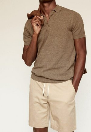 Polo de punto marrón, mangas cortas, con cuello. Pantalones cortos beige con cintura de cordón. Textura suave, ajuste relajado, sin patrones o detalles visibles.