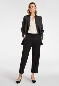Grijze blazer met zwarte revers, crèmekleurige blouse en zwarten op maat gemaakte broek. Schoenen hebben een strikdetail. Schone lijnen en een getailleerde silhouet.