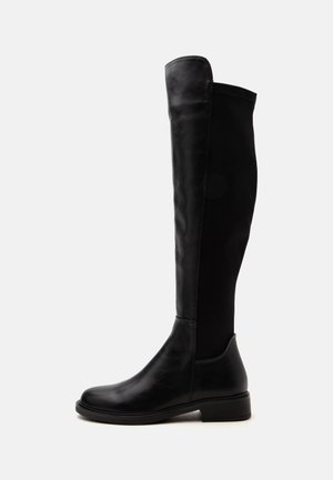 Botte haute noire en cuir et tissu jusqu'au genou avec un petit talon et un bout arrondi, vue de côté sur fond blanc.