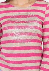 Langärmliges Oberteil mit pinkfarbenen und beigen horizontalen Streifen, das in der Mitte ein glitzerndes, kreisförmiges Logodesign aufweist. Weicher, strukturierter Stoff.