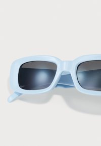 Gafas de sol azul claro con un marco cuadrado, lentes oscuros, acabado de plástico suave y brazos rectos y delgados.