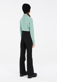 Maglione in pile verde chiaro con colletto, abbinato a pantaloni neri a fantasia. Un berretto nero e stivali neri spessi completano il look.