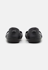 Paire de chaussures en cuir noir à enfiler vue de dos avec une petite étiquette de marque sur chaque talon.