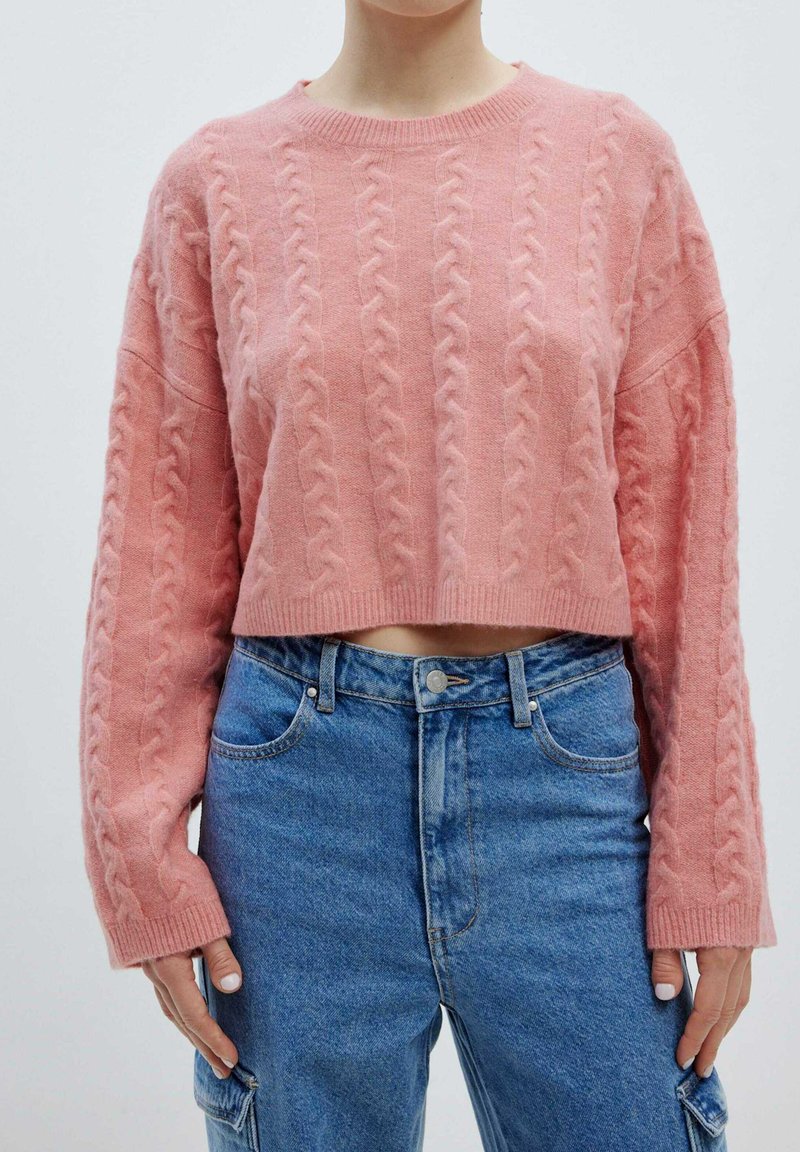 Rosa, kabelgestrickter, kurz geschnittener Pullover mit langen Ärmeln und strukturiertem Design, kombiniert mit hochgeschnittenen blauen Jeans.