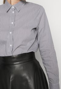 Musta-valkoisia raidallisia nappipaitoja kauluksella, pitkät hihat ja valkoiset napit, yhdistettynä mustaan korkeavyötäröiseen nahkahameeseen.