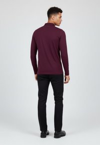 Bordeaux pitkähihaista polo-paitaa rakenteellisella kauluksella, sileällä pinnalla ja logolla selässä, yhdistetty mustiin tiukasti istuviin housuihin.