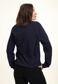 Námořnická modrá mikina vyrobená z měkké tkaniny s dlouhými rukávy a kulatým výstřihem. Má přiléhavý střih a jednoduchý design.