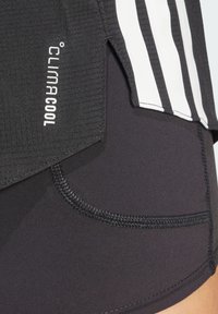 Haut de sport noir en tissu texturé, avec des accents de rayures blanches et le logo "Climacool", associé à un short noir ajusté et des détails de couture.