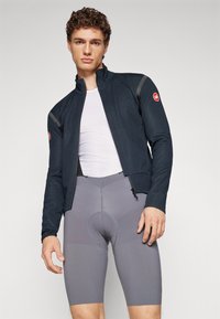 Men's cycling jacket in navy with a high collar, paired with gray cycling shorts featuring a padded seat and textured accents.