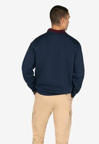 Felpa blu navy con collo borgogna, caratterizzata da una vestibilità comoda e maniche lunghe, abbinata a pantaloni cargo beige con tasche laterali.