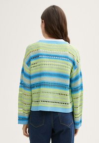 Stickad tröja med lös passform, prydd med växelvis blå och grön horisontell randning och hälldragstecken, avslutad med en blå rund halsringning.