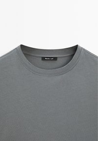 Grå bomulds t-shirt med rund hals og korte ærmer, med et lille sort mærke med "Massimo Dutti" ved kraven.