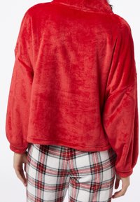 Pullover rosso peloso con una texture morbida, vestibilità ampia e maniche lunghe. Abbinato a pantaloni da pigiama a quadri bianchi e rossi con un motivo a scacchi.