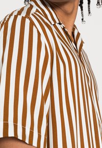 Korte mouw shirt met afwisselend bruine en witte verticale strepen, gemaakt van gestructureerde stof met een klassieke kraag en knoopsluiting.