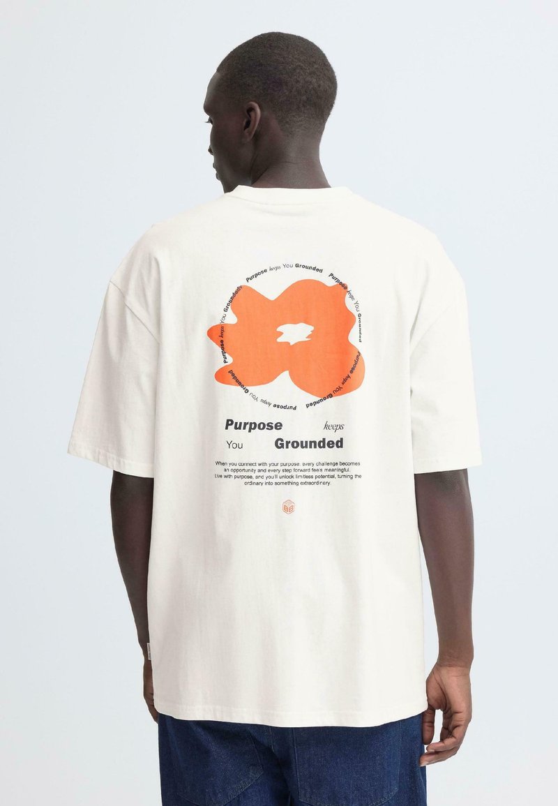 Cremefarbenes Baumwoll-T-Shirt mit einem abstrakten orangen Grafikmotiv und Text auf der Rückseite, mit lockerer Passform und kurzen Ärmeln.