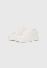 White sneakers with a smooth leather exterior, rounded toe, and flat rubber sole. Subtle perforations along the side for ventilation.