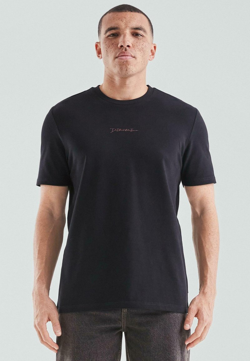 Schwarzes T-Shirt mit kurzen Ärmeln aus weichem Material, mit einem dezenten pinken Logo auf der Brust. Einfaches, klassisches Design mit rundem Ausschnitt.