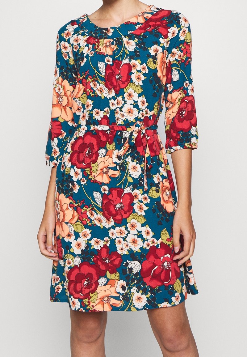 Blumenkleid mit blauem Hintergrund und roten sowie Pfirsichblüten. Dreiviertelärmel, runder Ausschnitt und passender Gürtel.