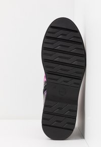 Semelle de chaussure en caoutchouc noir avec un motif zigzag texturé pour l'adhérence. Partie supérieure en textile coloré partiellement visible, présentant un design floral.