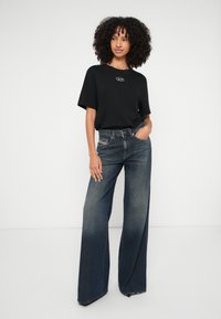 Μαύρο T-shirt με λογότυπο, συνδυασμένο με σκούρο τζιν παντελόνι με φαρδιά γραμμή, ψηλή μέση, που διαθέτει ξεθωριασμένη υφή και αντιθετικές ραφές.