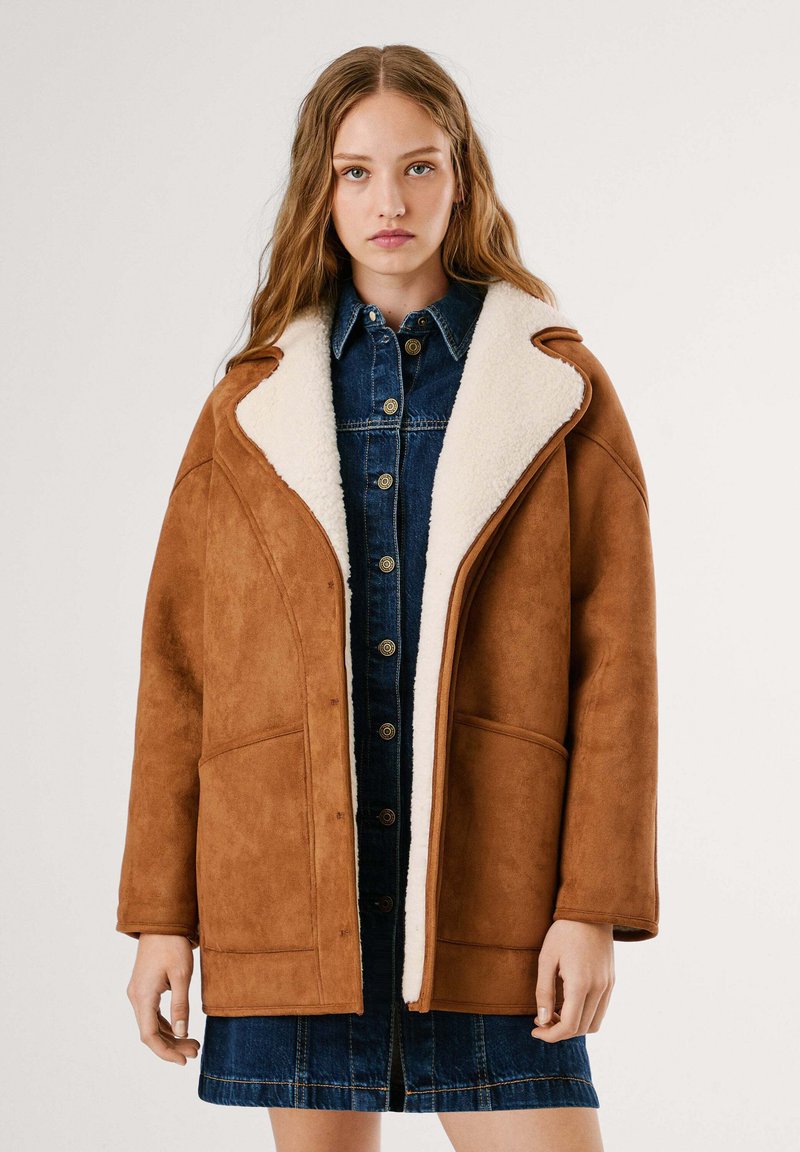 Cappotto in suede marrone con colletto in shearling bianco, vestibilità oversize, con tasche anteriori e un vestito in denim a bottoni sotto.