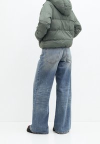 Puffet grøn hættejakke med vandret syninger; lyseblå brede jeans med en falmet tekstur; mørkebrune sko med flad sål.