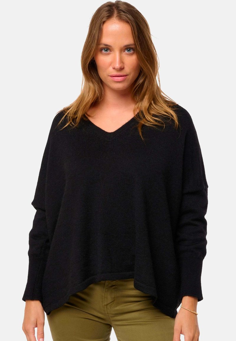 Schwarzer V-Ausschnitt-Pullover mit lockerer, oversized Passform, gerippter Textur und herunterhängenden Ärmeln. Kombiniert mit olivegrünen Hosen.