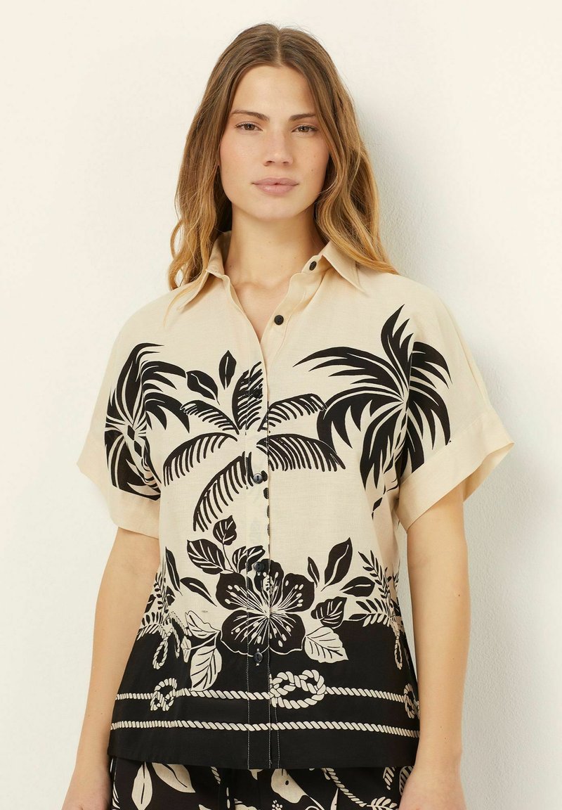 Crème overhemdsblouse voorzien van zwarte tropische bladeren en bloemenprints, korte mouwen en een zoom met een touwpatroon.
