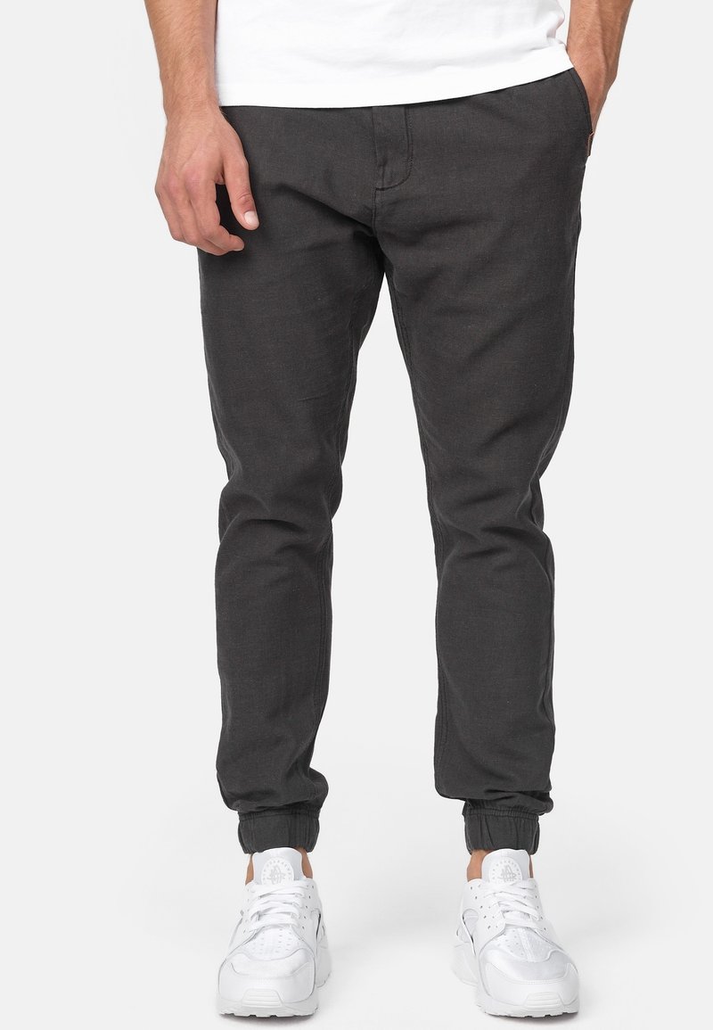 Donkergrijze joggerpants van zacht materiaal, met een elastische tailleband en boorden. Gepaard met witte sportschoenen.