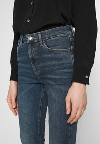 Skinny jeans i mörk tvättad denim, med fem fickor, en silverfärgad knapp och subtila sömdetaljer. Kombineras med en svart långärmad tröja.