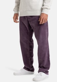 Lilla corduroy bukser med bred ben design, paret med hvite sneakers og en grå hettegenser. Har teksturert stoff og sidelommer.