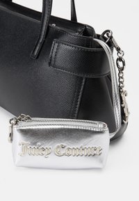 Czarna torebka teksturowana z podwójnymi uchwytami obok srebrnego, metalicznego mini woreczka z wytłoczonym na złoto napisem "Juicy Couture". Oba przedmioty mają zamki błyskawiczne.