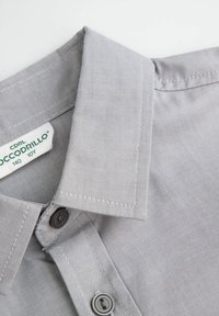 Kołnierzyk koszuli z szarego materiału z pionowym wzorem pasków, ozdobiony czarnymi guzikami i metką z informacjami o marce oraz rozmiarze.