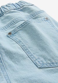 Tessuto denim blu chiaro con una consistenza morbida. Presenta un elastico in vita e una singola tasca posteriore con dettagli in metallo sui bottoni.