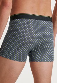 Boxer briefs in navy blue with a geometric pattern of white and yellow crosses. Features a black waistband with logo detailing.