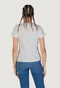 T-shirt bianco aderente con maniche corte, texture liscia e design minimal. Indossato con jeans in denim blu con tasche posteriori.