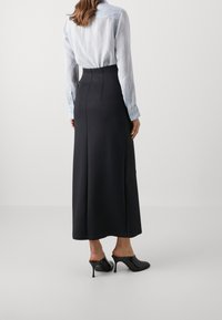 Svart maxikjol med figursydd midja, slät textur och detaljsömmar, kombinerad med en ljusblå skjorta med långa ärmar och svarta klackade mules.