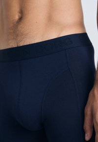 Marineblå boxershorts laget av elastisk stoff, med en jevn tekstur og elastisk linning med bølget logo.