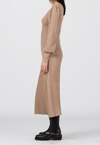 Pull en tricot côtelé marron clair avec manches bouffantes, associé à un pantalon large en simili cuir beige clair et des bottines noires.