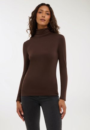 Maglione a maniche lunghe marrone con collo a imbuto realizzato in un tessuto liscio, design aderente e cuciture minime. Indossato con jeans scuri, caratterizzati da una silhouette classica.