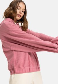 Pink hoodie with herringbone pattern, long sleeves, and a rounded hem. Made of textured fabric, featuring a kangaroo pocket and drawstring hood.