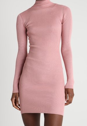 Robe près du corps à manches longues en maille côtelée rose poudrée, avec un col montant, portée par une personne debout sur un fond neutre.