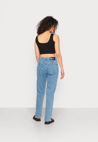Jeans de ganga azuis com um ajuste relaxado, cintura alta e dois bolsos traseiros. Combinados com uma camisola cropped preta.