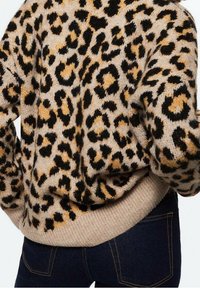 Sweter w panterkę na beżowym tle, ozdobiony czarnymi i pomarańczowymi plamami. Miękka faktura o luźnym kroju z prążkowanym dołem. Połączony z ciemnymi dżinsami.