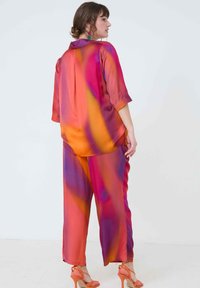 Satin co-ord set met een kleurrijke verloop van roze, oranje en paars. De top heeft een kraag en driekwartmouwen; de broek heeft een ontspannen pasvorm.