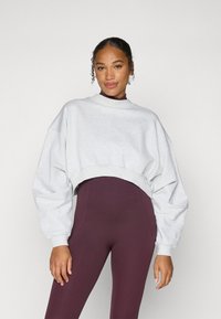 Lys grå croppet sweatshirt med høy hals og nedsenkede skuldre, kombinert med mørk burgunder leggings. Myk, teksturert stoff.