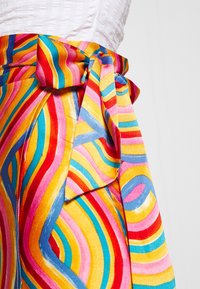 Jupe colorée avec des rayures ondulées audacieuses en rose, jaune, bleu et rouge. Elle dispose d'un détail de taille nouée. Texture de tissu lisse.