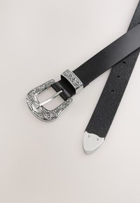 Cintura nera in pelle con fibbia ornamentale in argento. La fibbia presenta incisioni floreali. La cintura ha una finitura strutturata e una punta appuntita.