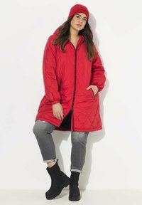 Red quilted long coat with a hood, front zipper, and side pockets. Paired with gray jeans and black ankle boots.